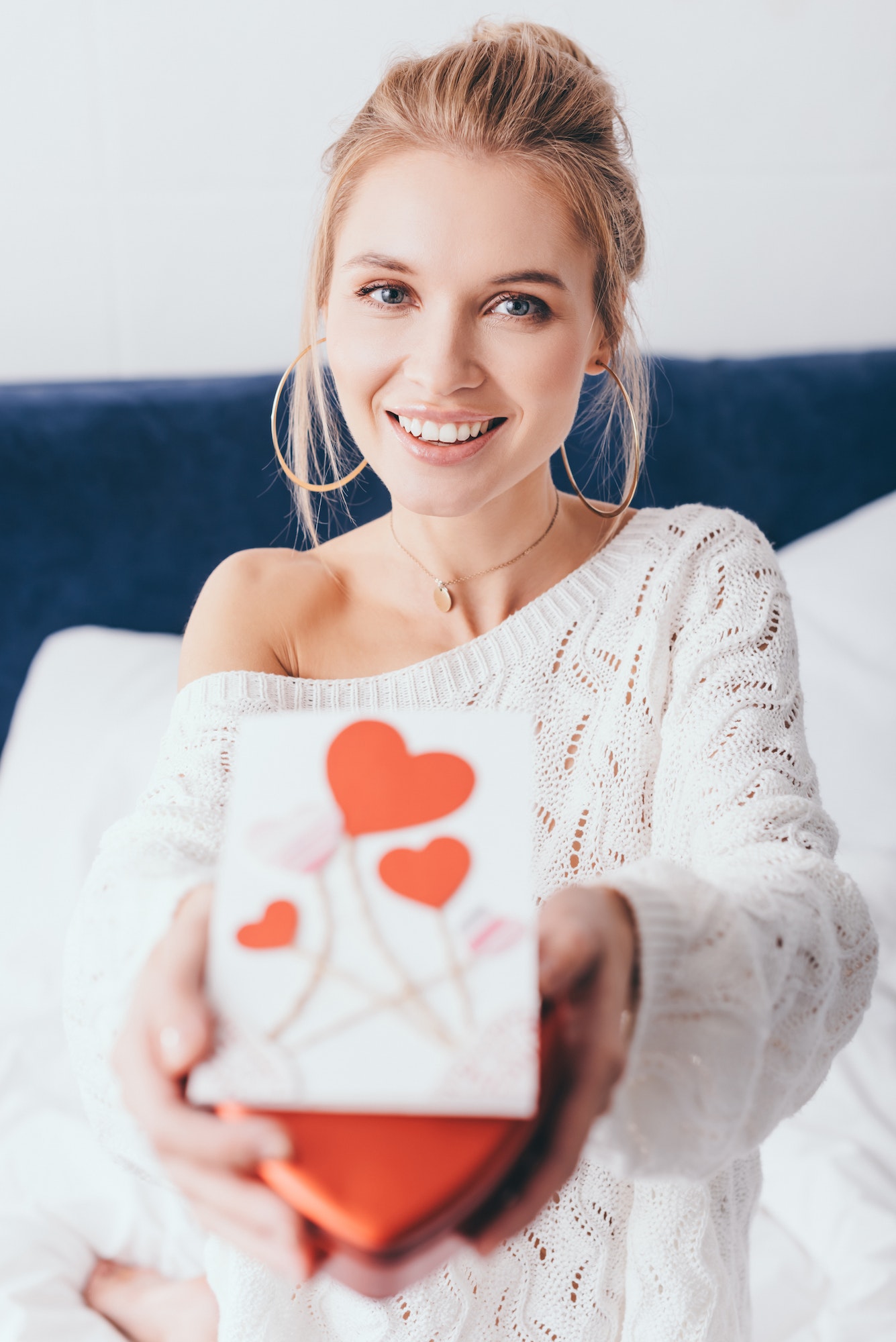 selective focus of happy woman holding gift box and valentine card on bed